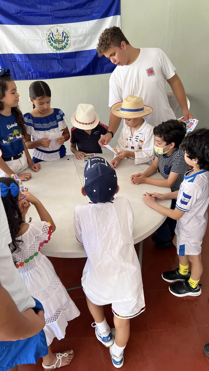 Learners in traditional Salvadoran dress beside the flag of El Salvador